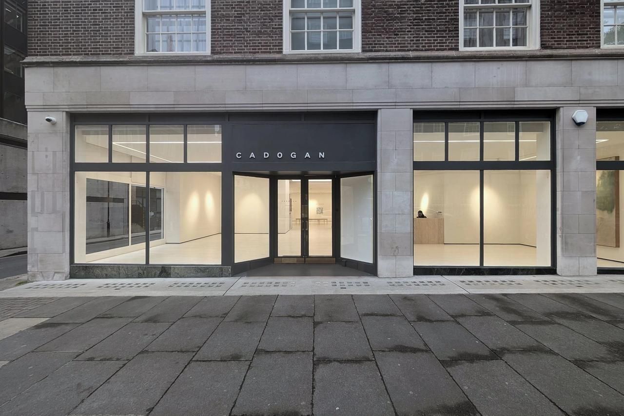 The full ground floor elevation at dusk, three lit bays under a dark grey fascia set into pale stone with brick above
