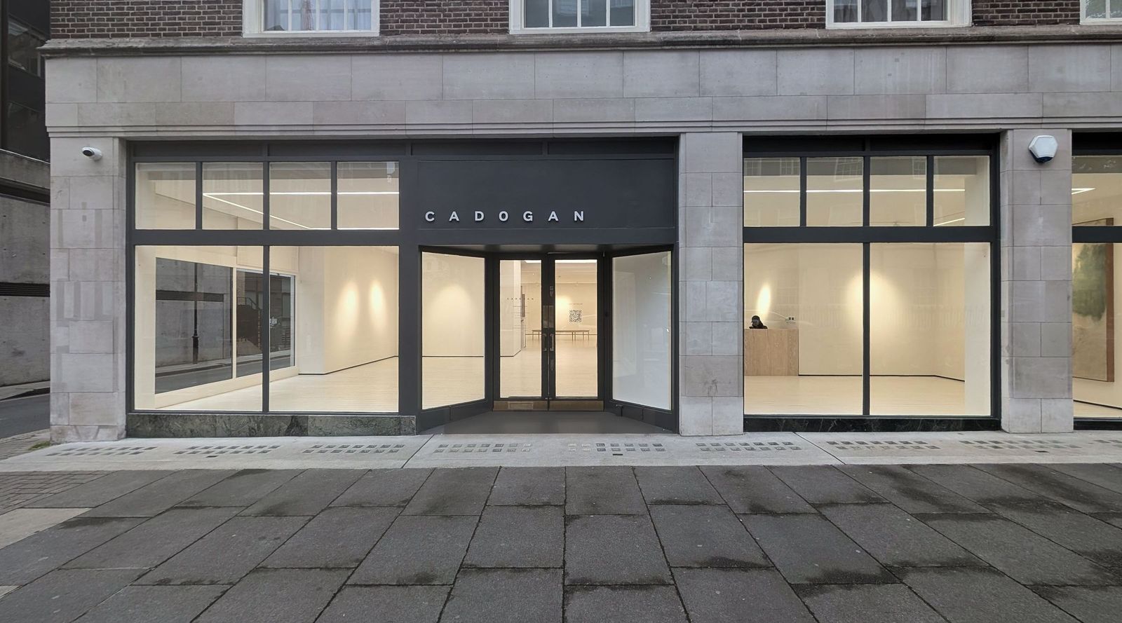 The full ground floor elevation at dusk, three lit bays under a dark grey fascia set into pale stone with brick above