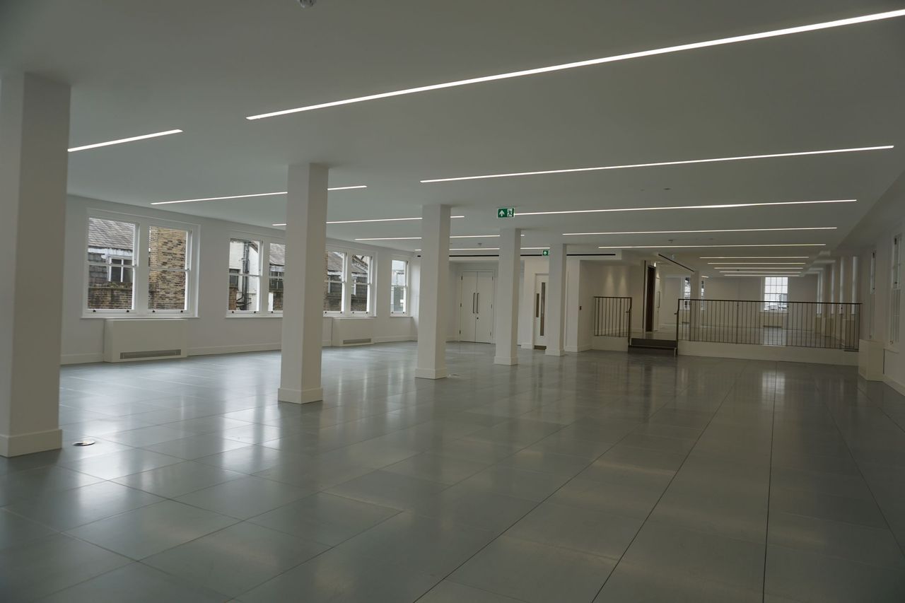 An open office floor after decoration, with white painted columns and soffits, a grey tiled floor and daylight down both sides