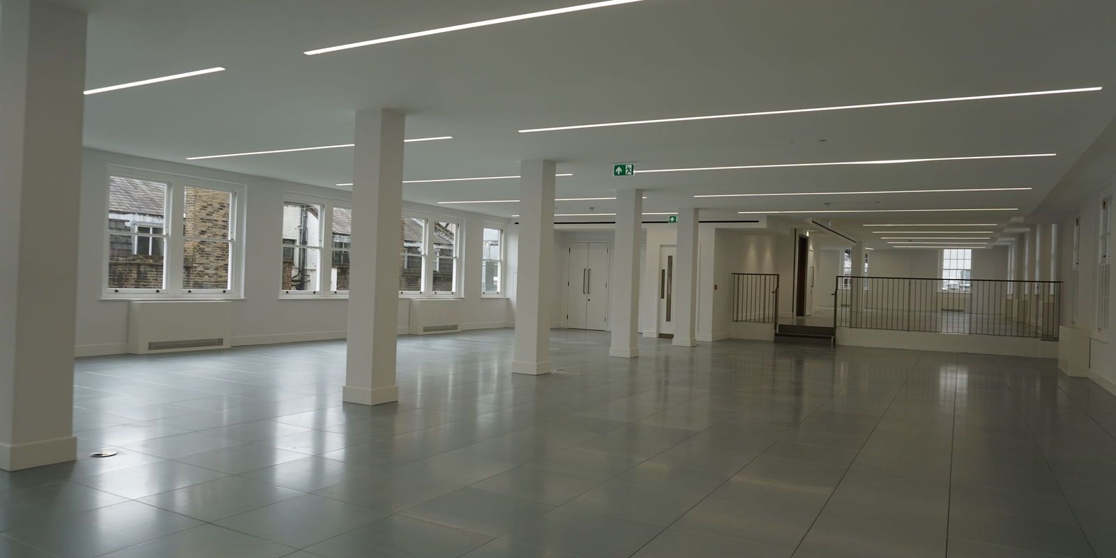 An open office floor after decoration, with white painted columns and soffits, a grey tiled floor and daylight down both sides
