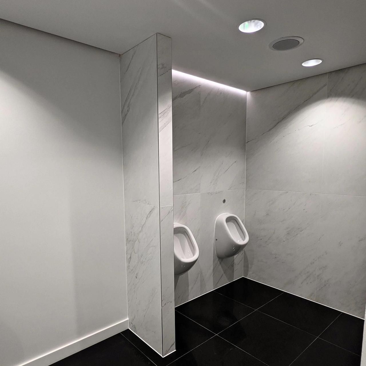 Urinal wall in marble-effect panels with a white painted ceiling and a lit cove