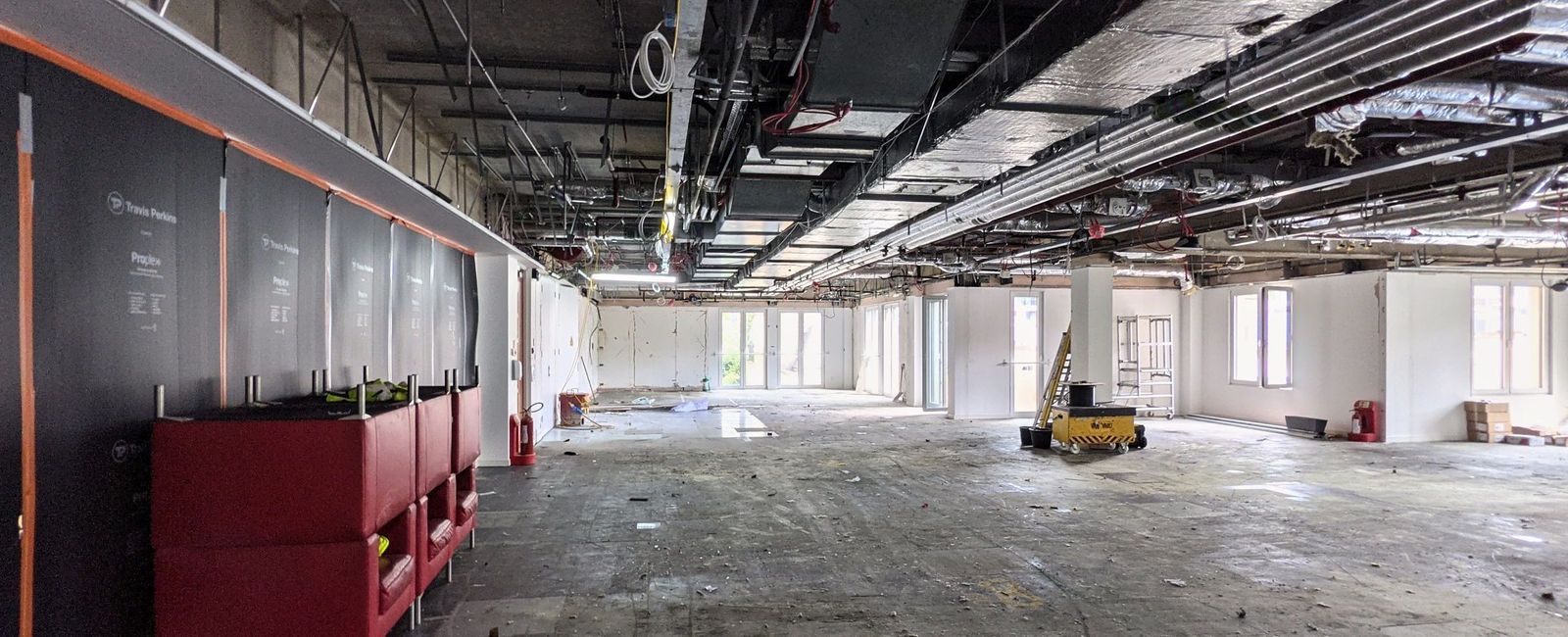 The office floor in August 2021 stripped to the slab with services exposed in the ceiling and red seating stacked along one wall