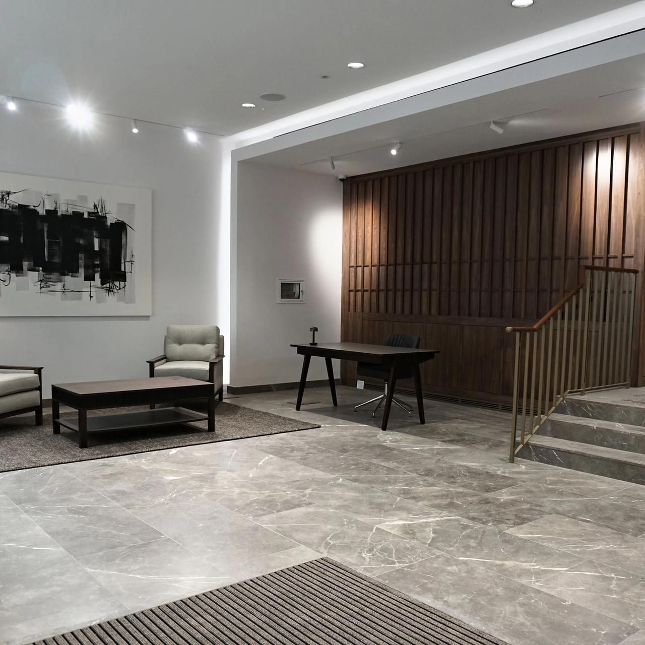 Reception with an abstract artwork on a white wall, walnut slatted screen and steps with a brass rail