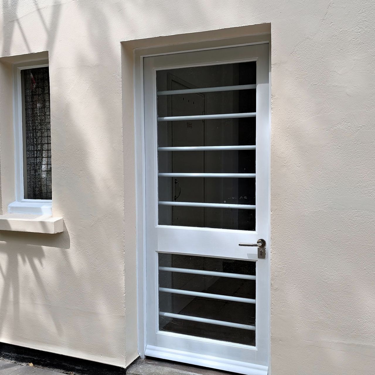 The same rear door repainted white in a clean rendered wall, the staining gone and the window reveal sharp
