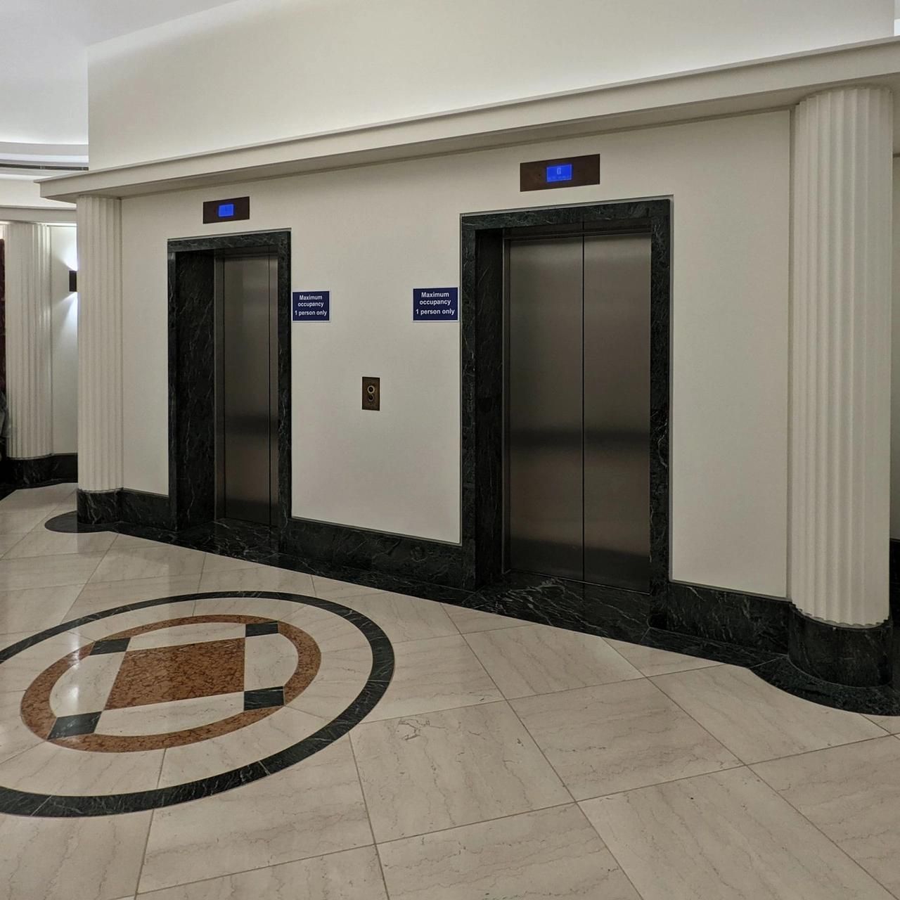 Lift lobby on 30 April 2021 with the walls under red sheeting, the lift doors closed and the terrazzo roundel uncovered