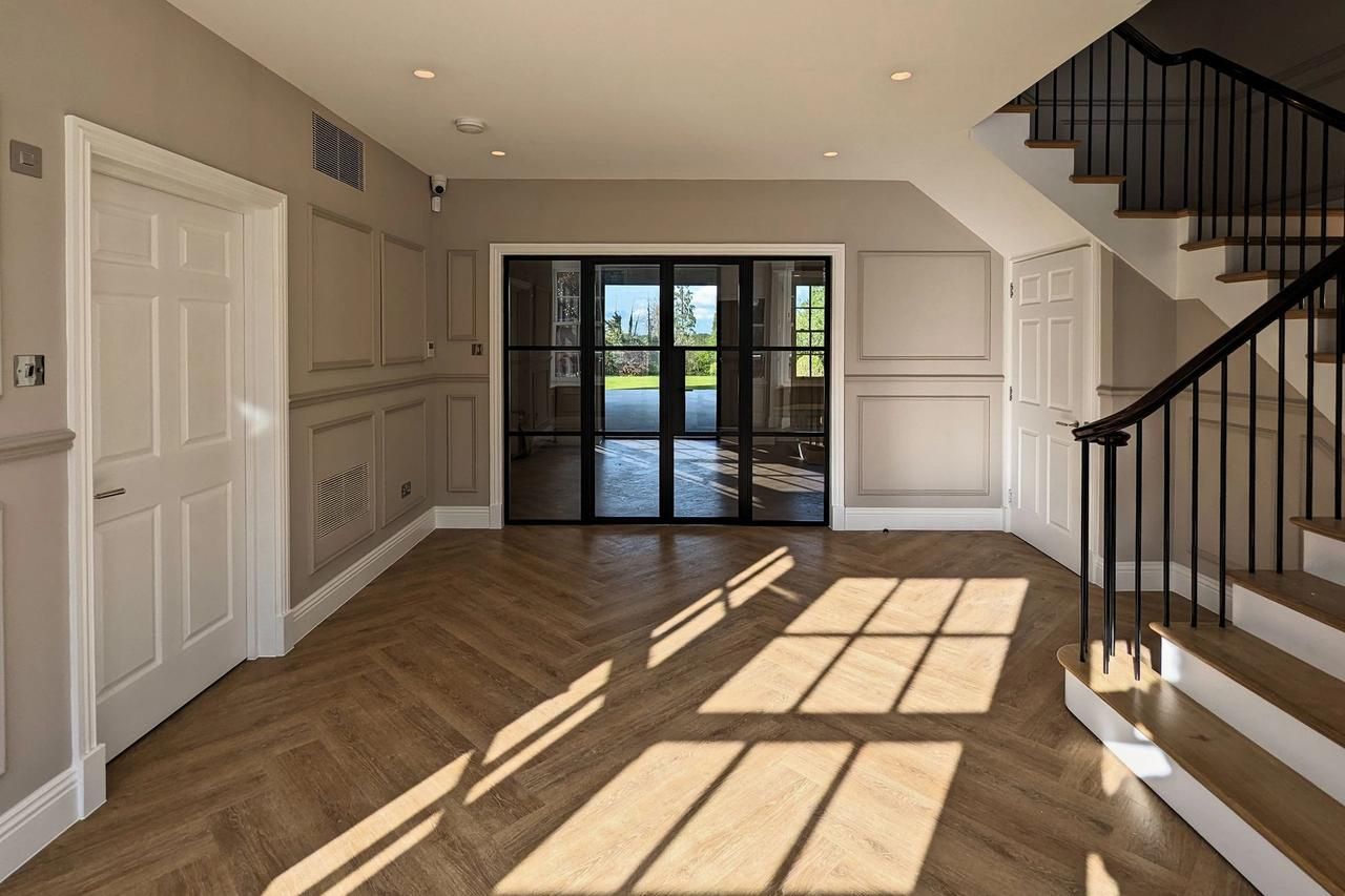 Panelled hall of a family house in Cuffley looking through black glazed steel doors to the garden, with afternoon light across a herringbone floor