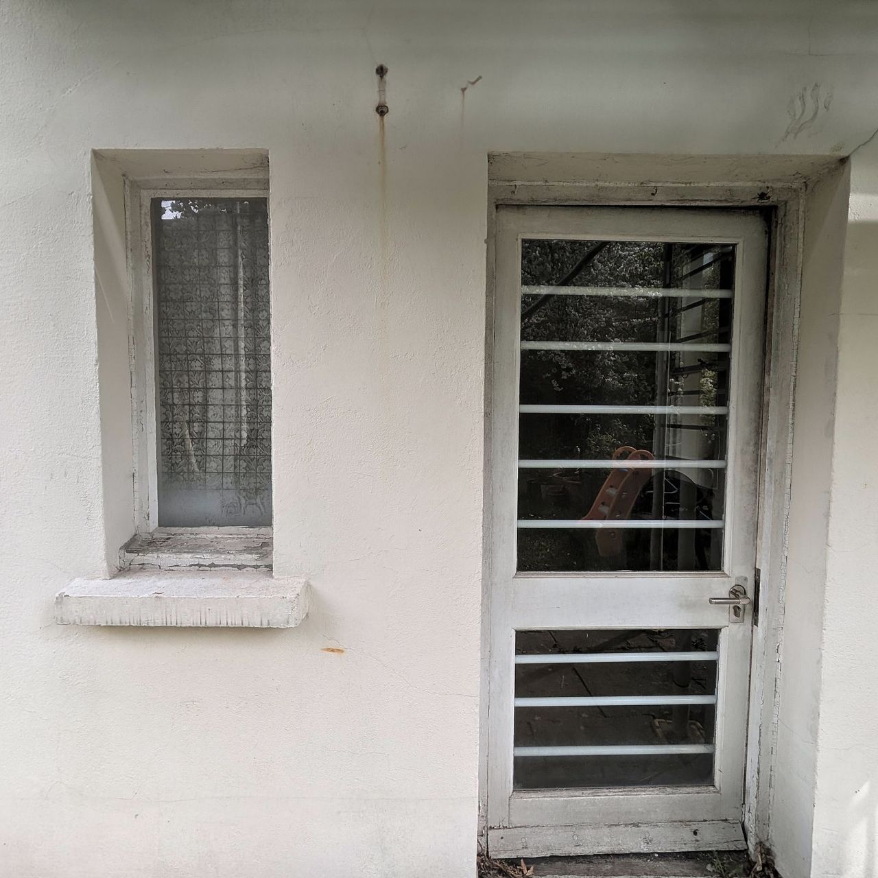 A glazed rear door with horizontal glazing bars in a painted rendered wall, a small window to the left and a rainwater pipe to the right