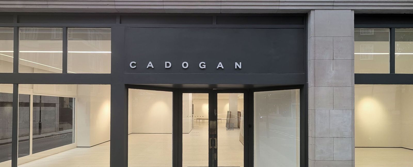 The finished shopfront lit from within at dusk, dark grey fascia with the gallery name in applied lettering