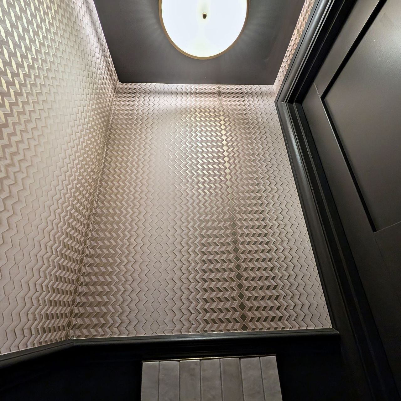 The same embossed chevron covering running up a sloping ceiling to a round flush ceiling light, against a dark panelled door