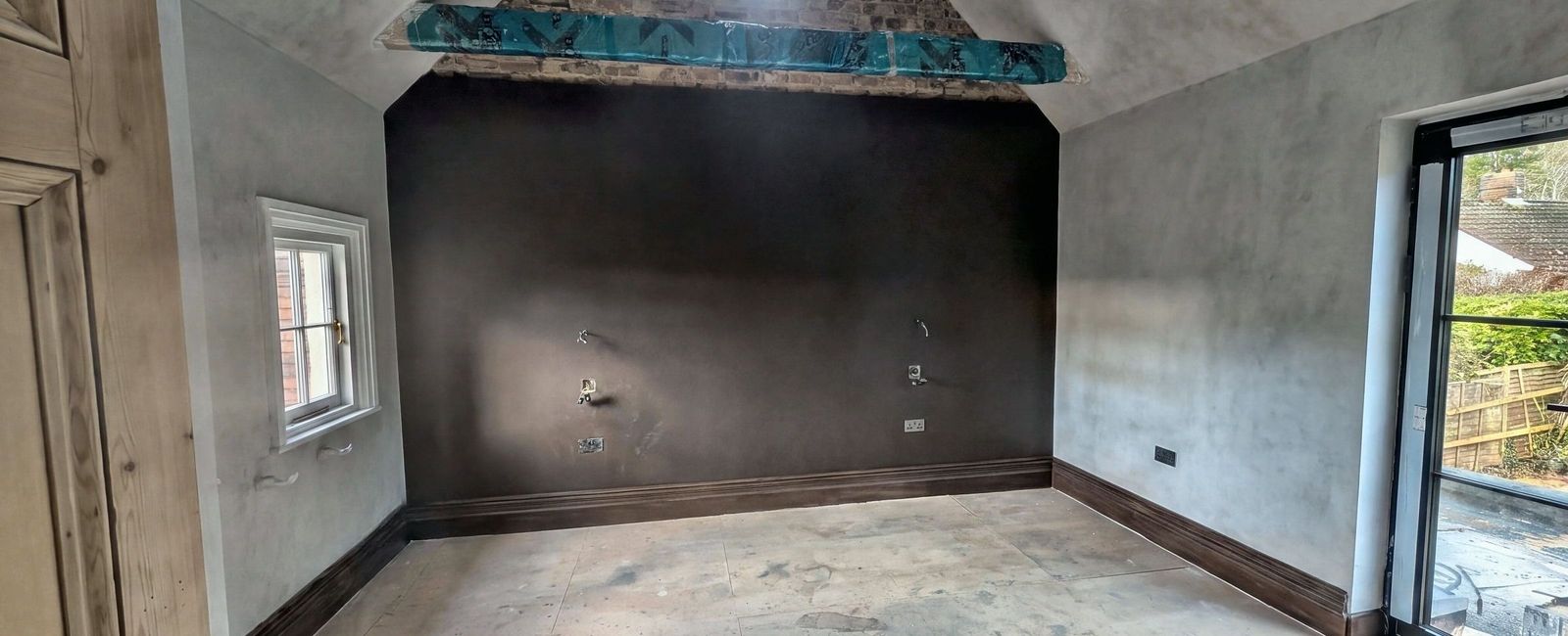 A room mid works with a dark painted chimney breast, roof timbers wrapped in blue protective film and floor protection down