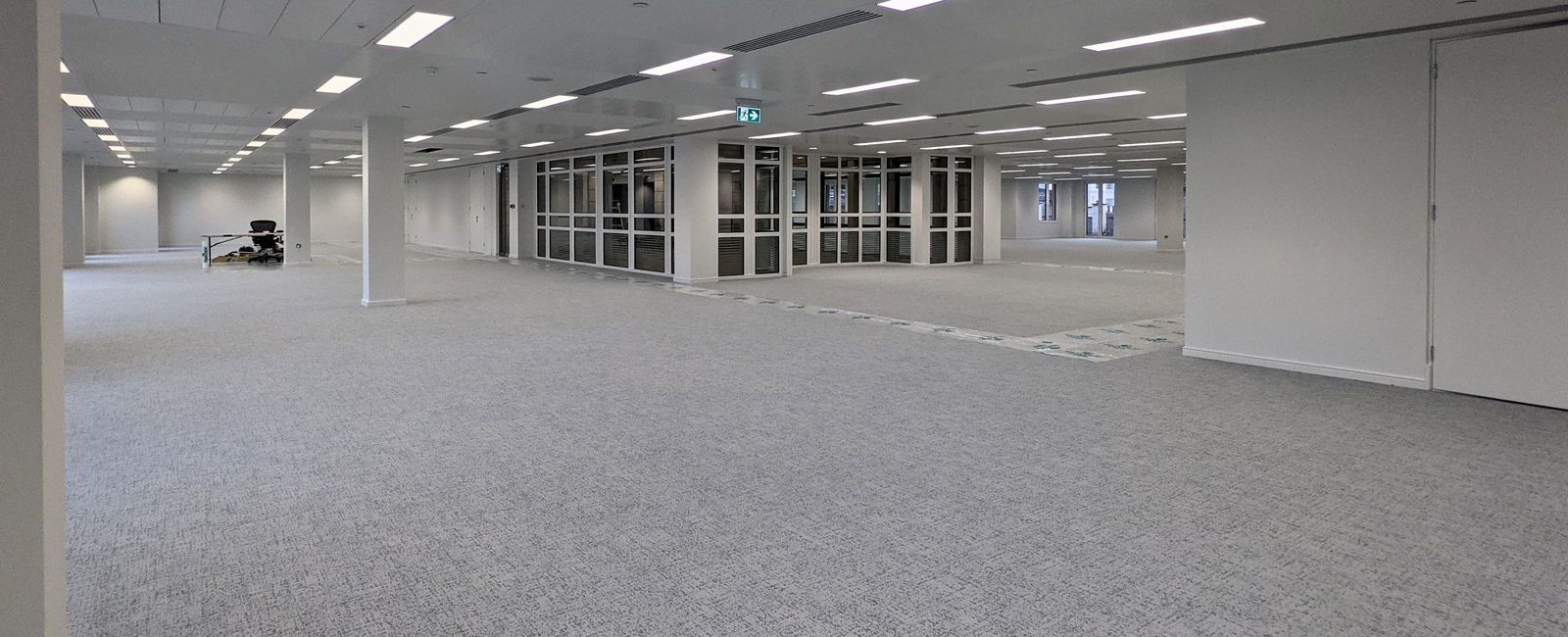Open plan office floor looking towards a glazed partition with white walls and ceiling tiles