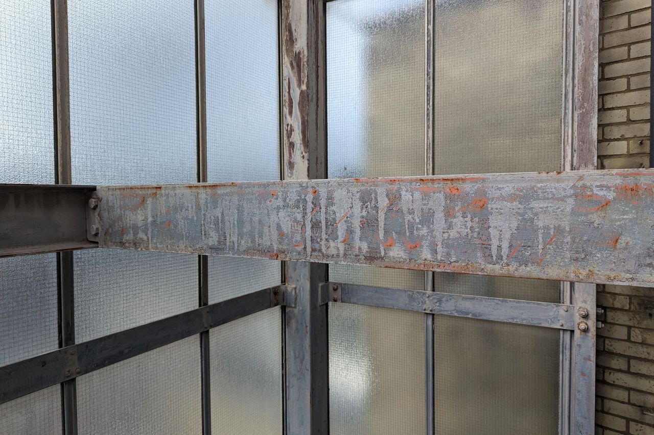An external steel fire escape before redecoration, with flaking paint and orange corrosion across a main beam and its bolted connections