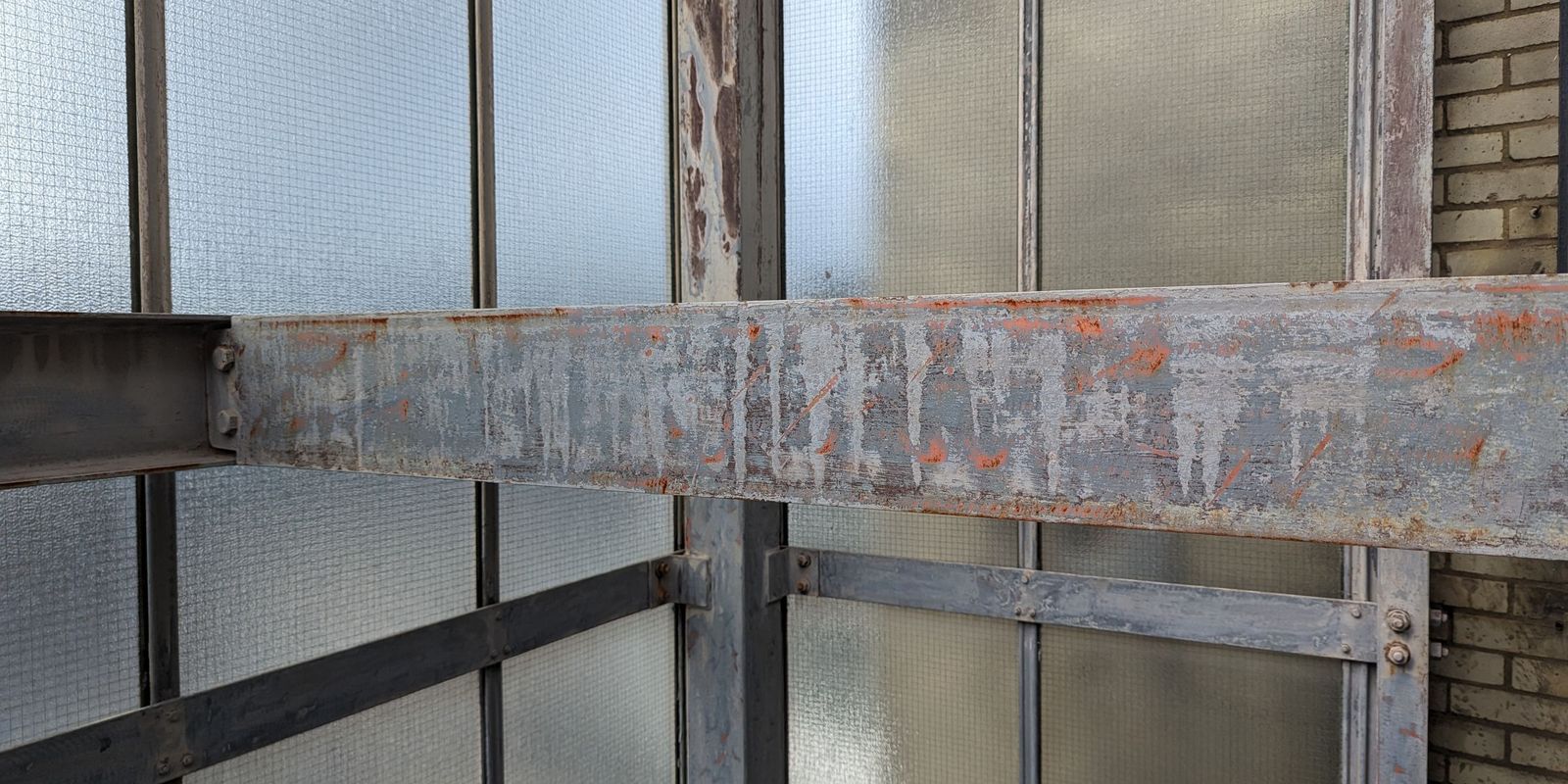 An external steel fire escape before redecoration, with flaking paint and orange corrosion across a main beam and its bolted connections
