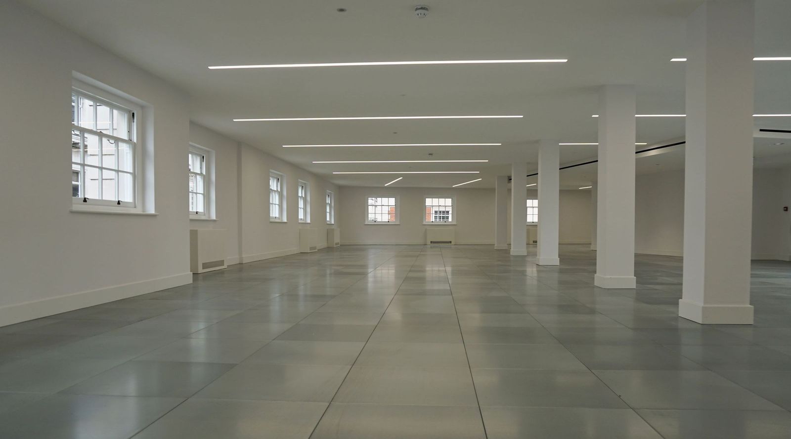 Finished office floor at Sackville Street with white walls and columns, a grey tiled floor and sash windows along both sides