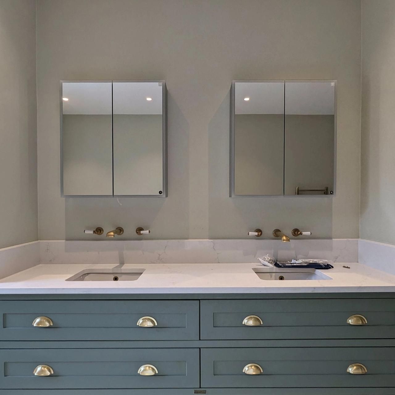 Master ensuite with a sage green vanity, twin mirrored cabinets and brass wall lights on a soft grey wall