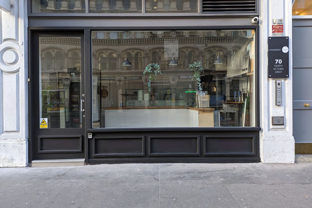 The shopfront square on, dark panelled stallriser under full height glazing between white painted pilasters