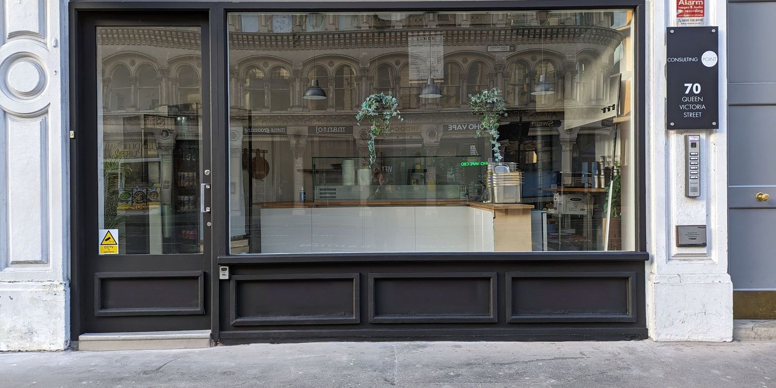 The shopfront square on, dark panelled stallriser under full height glazing between white painted pilasters