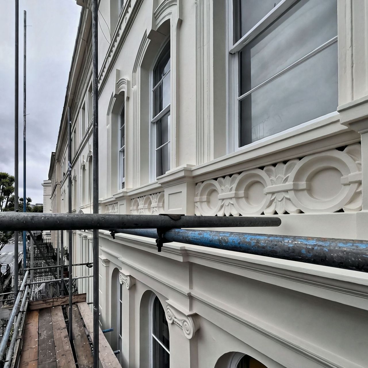 An enriched stucco band of linked ovals and carved leaves over a dentil course, running away along the finished elevation with the street below