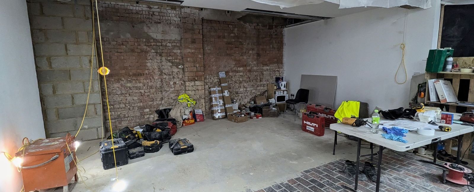 The interior during strip-out with exposed brick and blockwork, a brick paviour floor and polythene sheeting to the ceiling