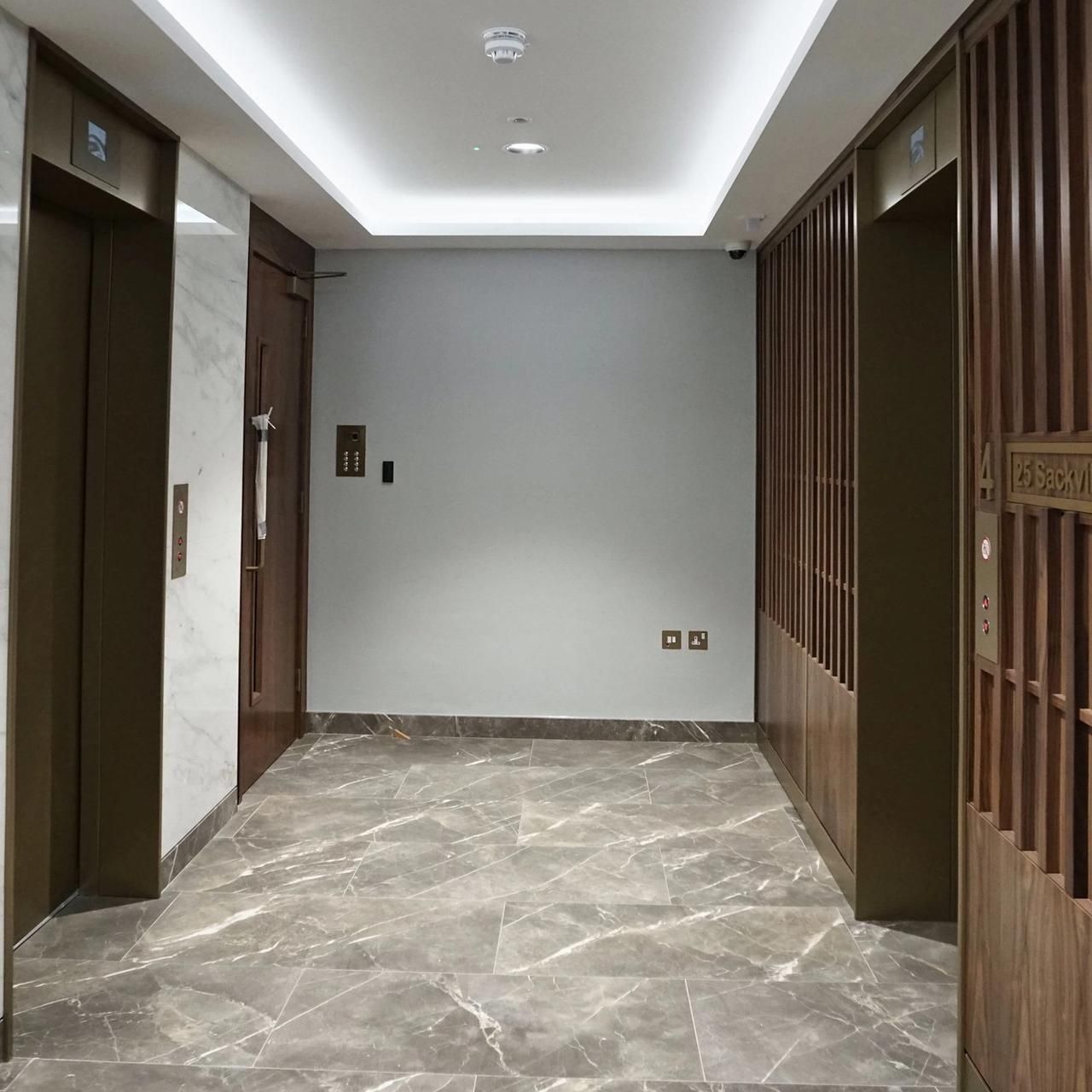 Lift lobby with marble walls, walnut slats, brass lift doors and a lit cove to the ceiling