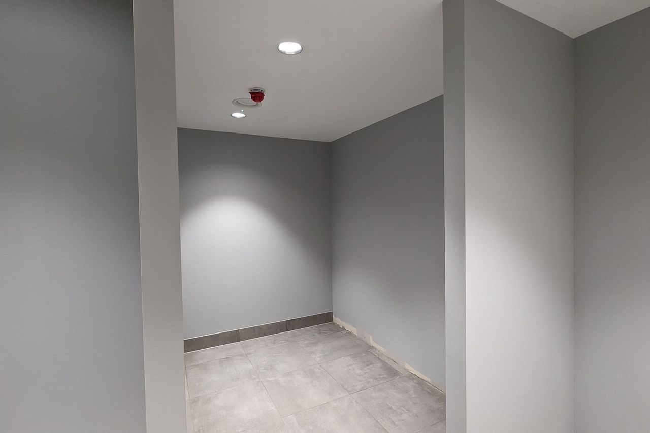 A finished communal area in grey, with a recessed downlight, a red ceiling sounder and a large format tiled floor