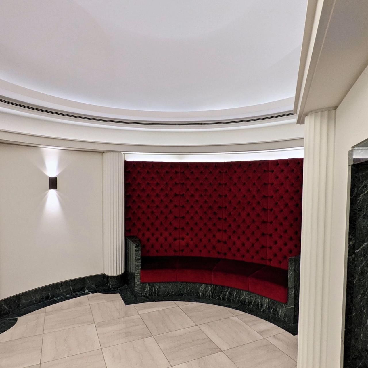 Curved alcove with a red velvet banquette, green marble plinth and fluted pilaster, painted walls above