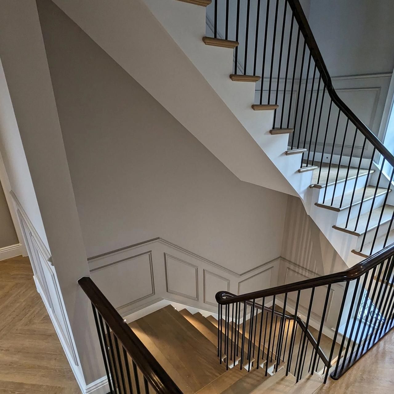 The stair from below, painted panelling on the wall and a dark timber handrail on black metal balusters