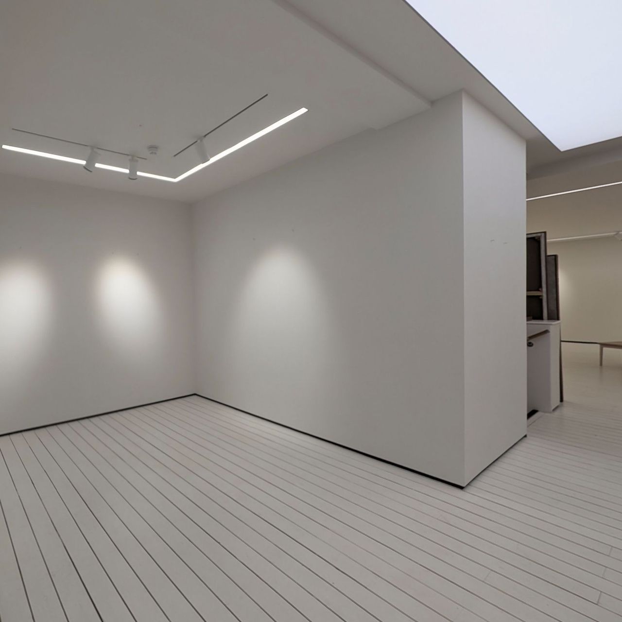 The upper gallery from the stair head, a white display wall meeting the painted boarded floor with a rooflight above