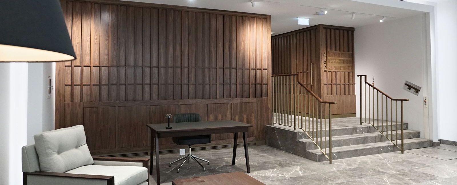 Reception at Sackville Street with walnut slatted panelling, a brass handrail on the steps and two armchairs on a marble floor