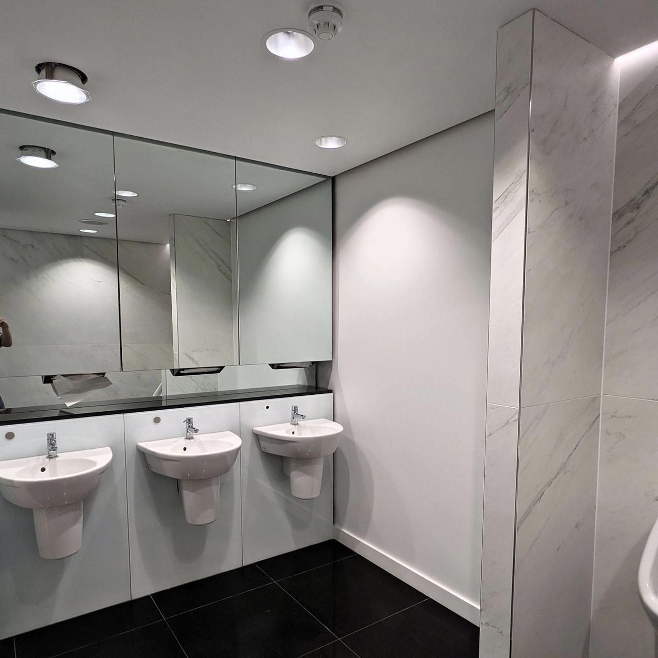 Finished WC with three basins under a long mirror, marble-effect wall panels and a black tiled floor