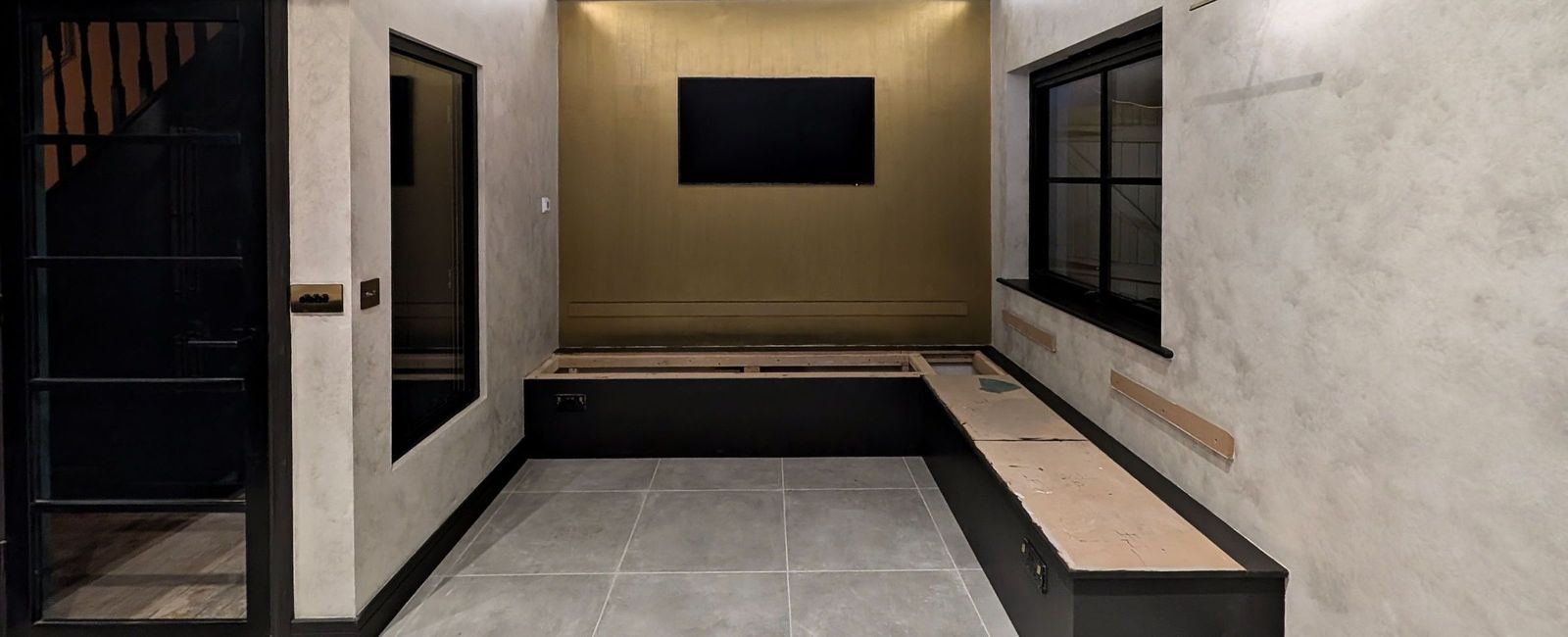 Pale mottled walls under a continuous cove light, an olive gold end wall with a wall mounted television and banquette seating below