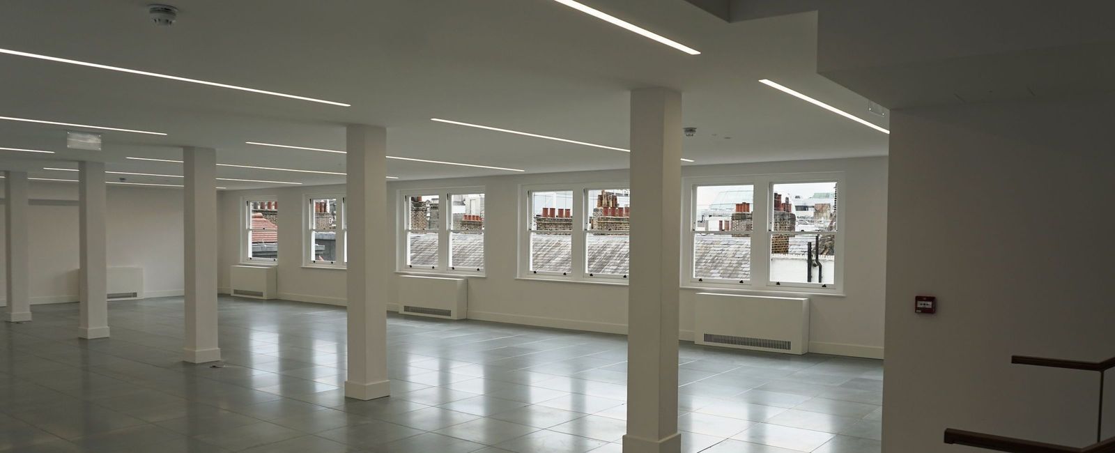 Open office floor with white columns, a grey tiled floor and windows along the far wall, May 2023