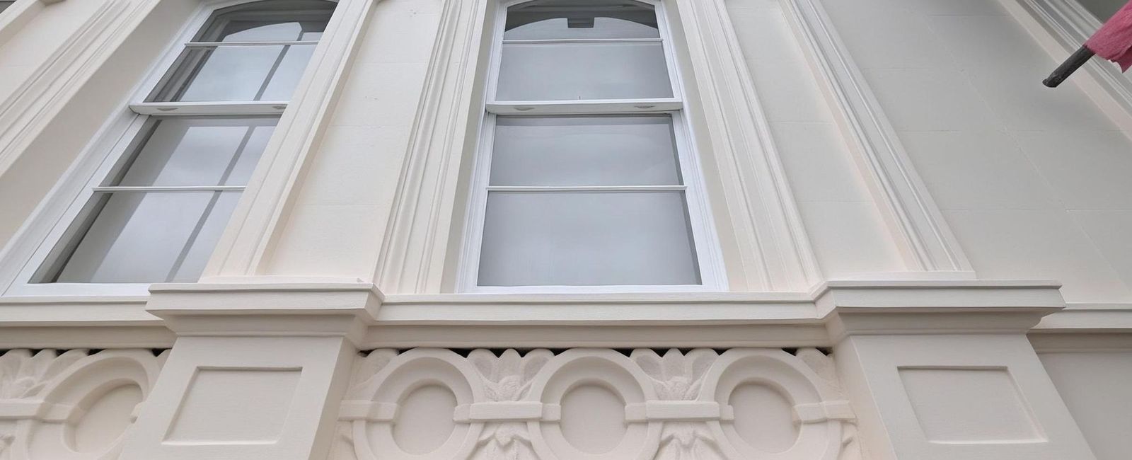 Two arched sash windows in moulded stucco surrounds with keystones, and beneath them an enriched band of linked ovals and carved leaves over a dentil course, freshly painted