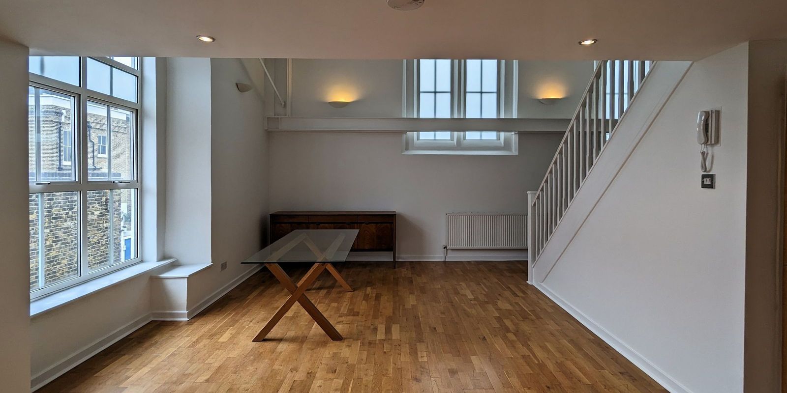 A double height room with arched clerestory windows, white walls and a pale timber floor, the stair rising to the right