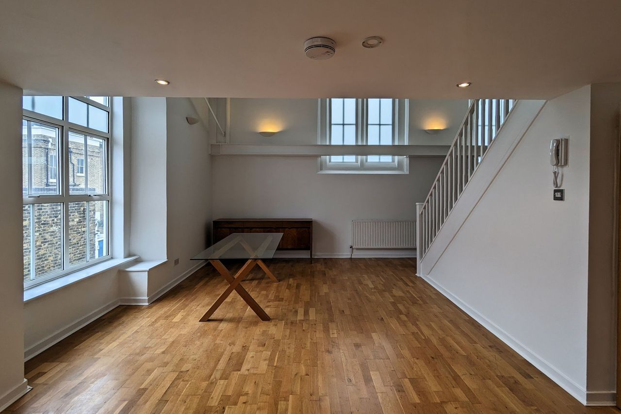 A double height room with arched clerestory windows, white walls and a pale timber floor, the stair rising to the right
