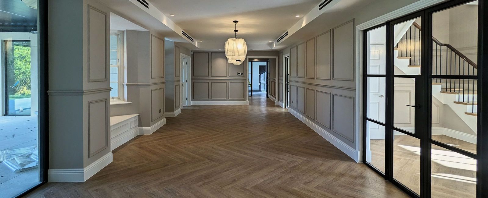 Long ground floor hallway with dado-height panelling on both sides, glazed steel doors and a pendant light