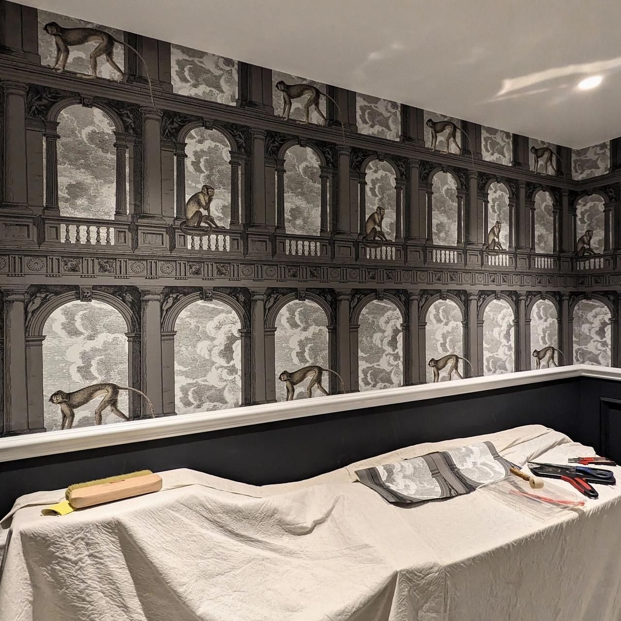Downstairs WC mid-way through papering, the architectural pattern going up above dark panelling with dust sheets over the basin