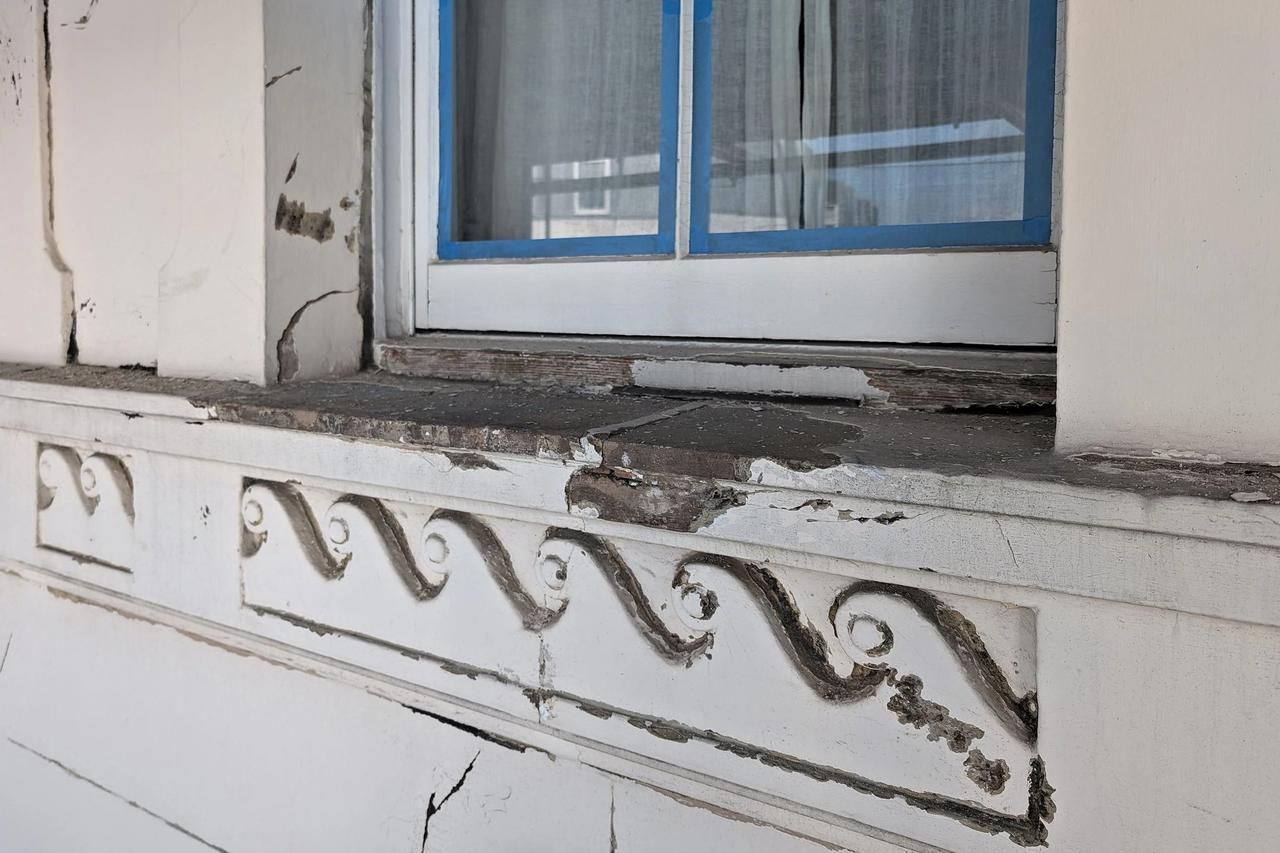 A Vitruvian scroll enrichment band on a stucco front, photographed before repair, with paint loss, cracking and dark staining across the run