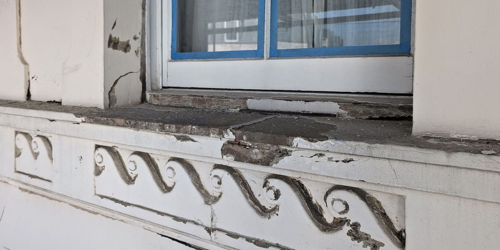 A Vitruvian scroll enrichment band on a stucco front, photographed before repair, with paint loss, cracking and dark staining across the run