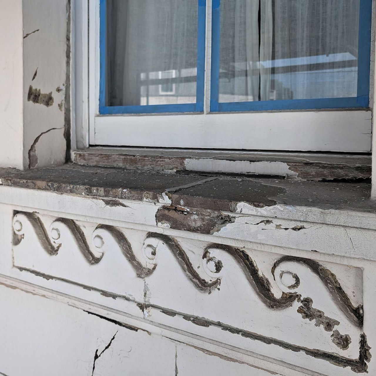 A moulded scroll band beneath a window, cracked through and losing its profile, with a painted sash above
