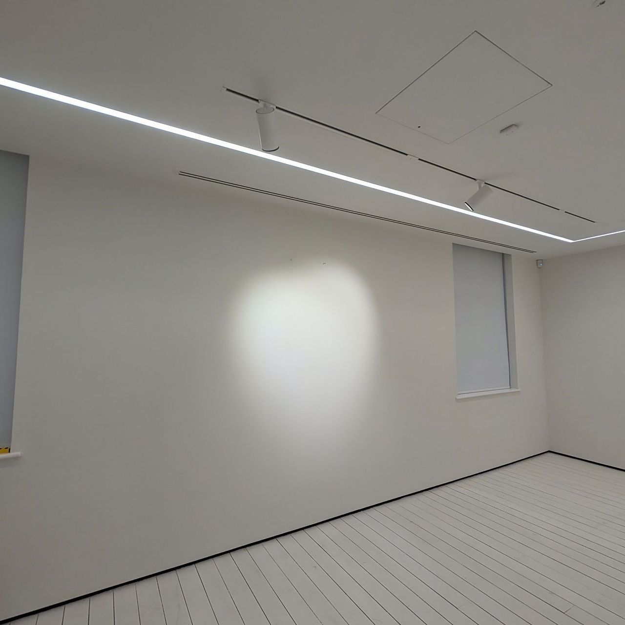 A corner of the upper gallery with wall washers raking across white and a blind recess to the window wall