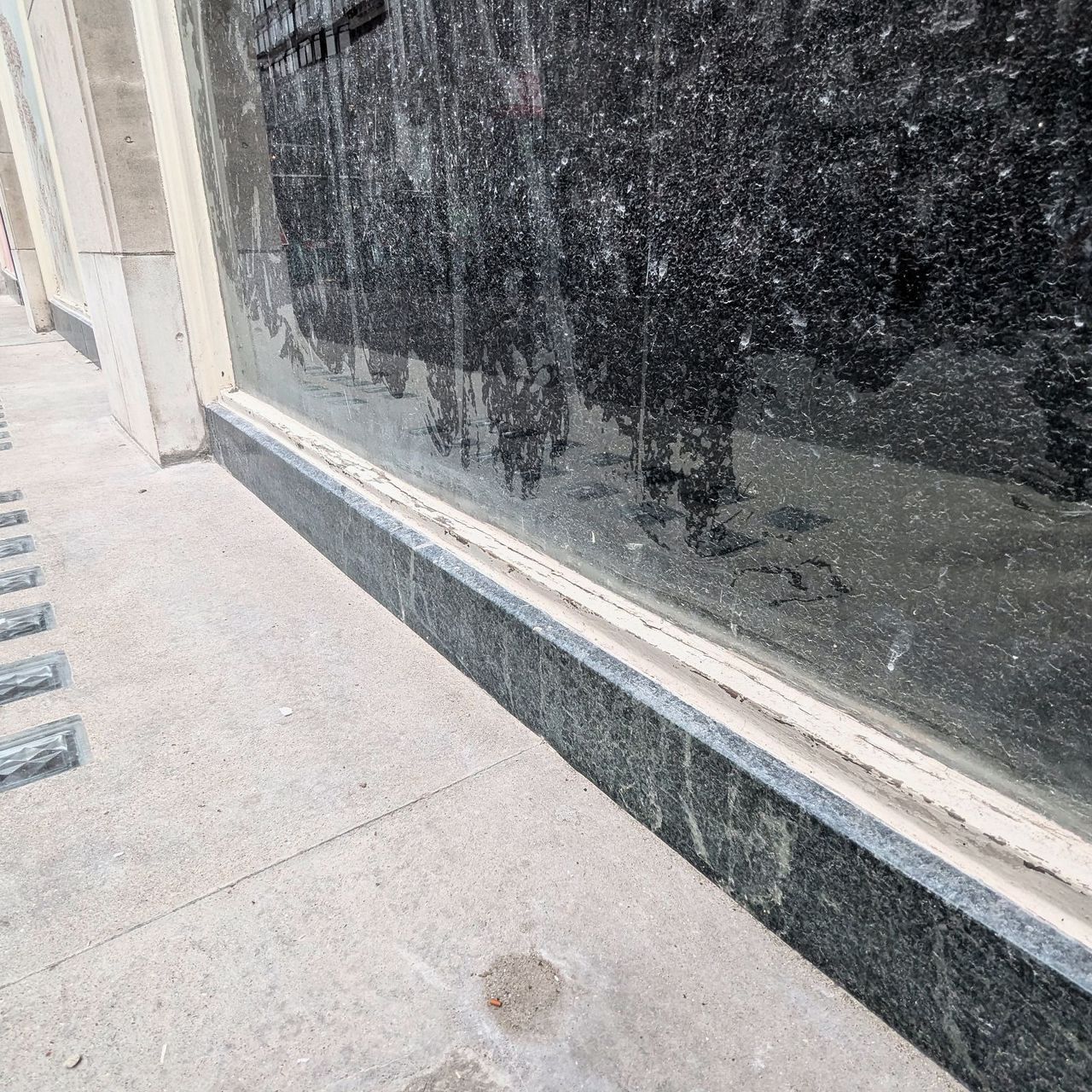 Blacked-out shop glazing heavily streaked with dirt above a dark green stone stallriser