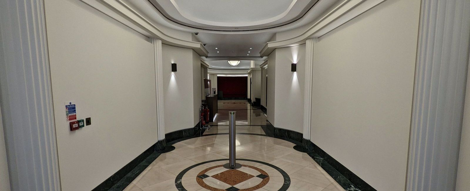 Art deco corridor with fluted pilasters either side, a terrazzo roundel in the floor, green marble plinths and a pendant light