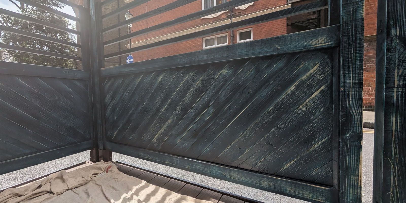 A weathered panel with the coating broken down to bare grey timber and green discolouration across the boards