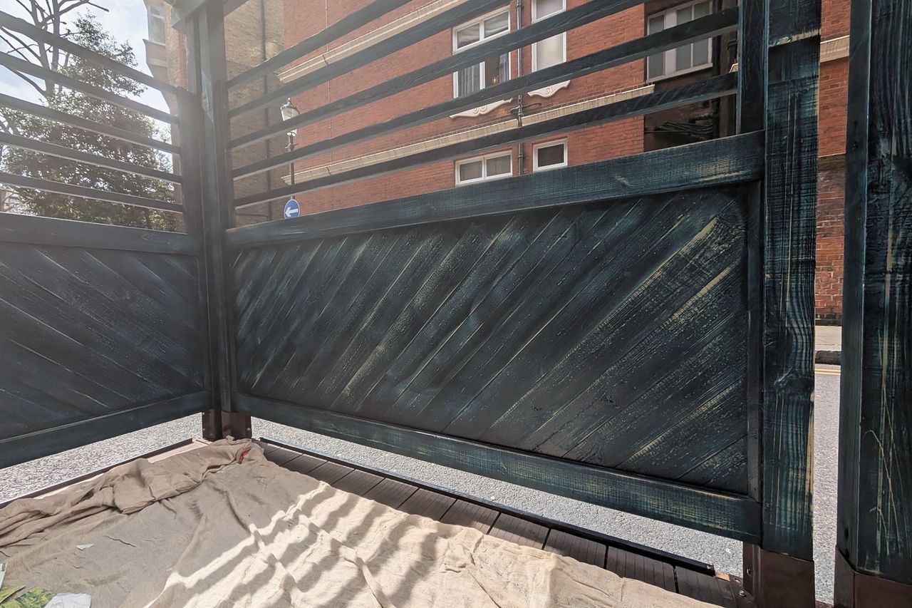 A weathered panel with the coating broken down to bare grey timber and green discolouration across the boards