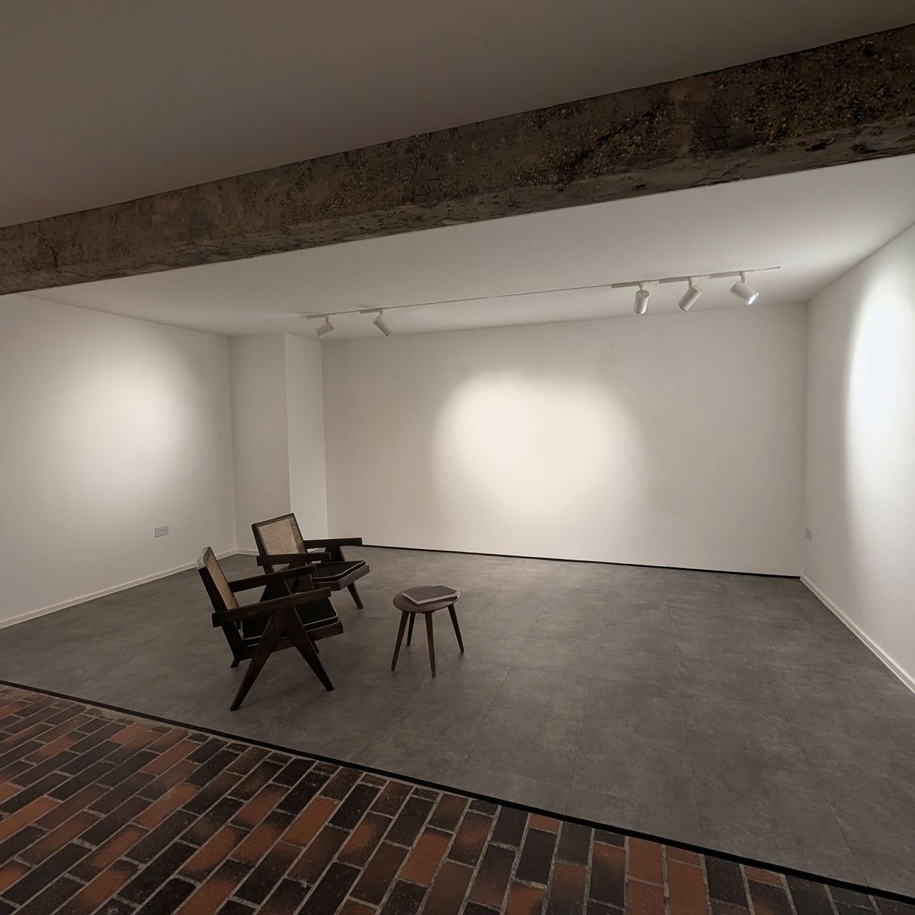 The lower gallery from the opposite corner, white walls washed by track spots above a brick paviour and screed floor