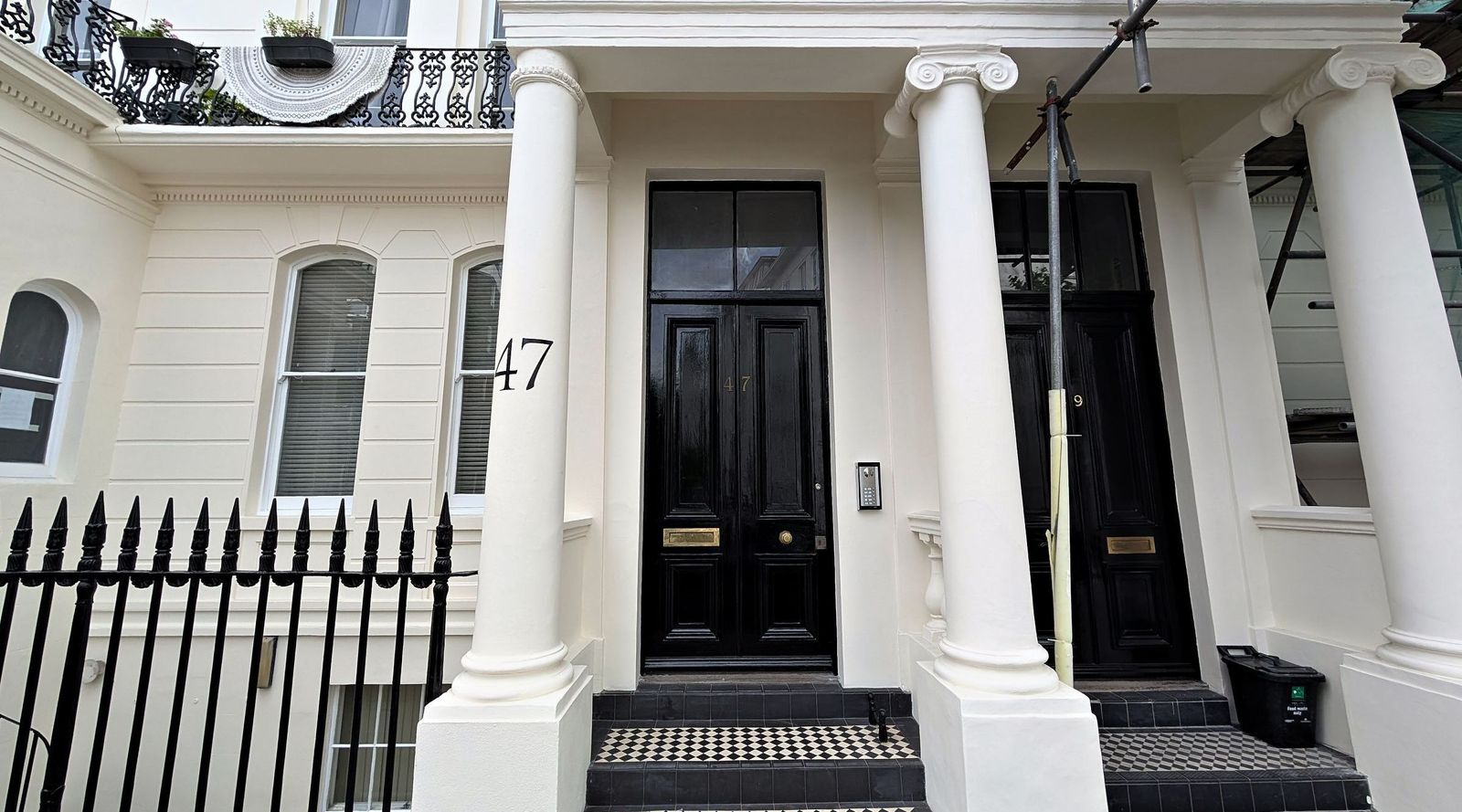 The entrance of a restored stucco terraced house from the street: paired Ionic columns, black double doors, tiled steps and black iron railings, with the restored terrace running away behind.