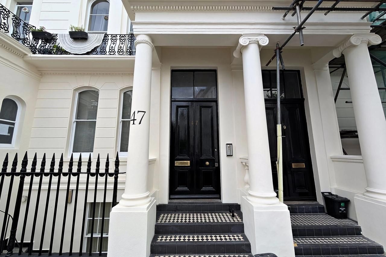 The entrance of a restored stucco terraced house from the street: paired Ionic columns, black double doors, tiled steps and black iron railings, with the restored terrace running away behind.