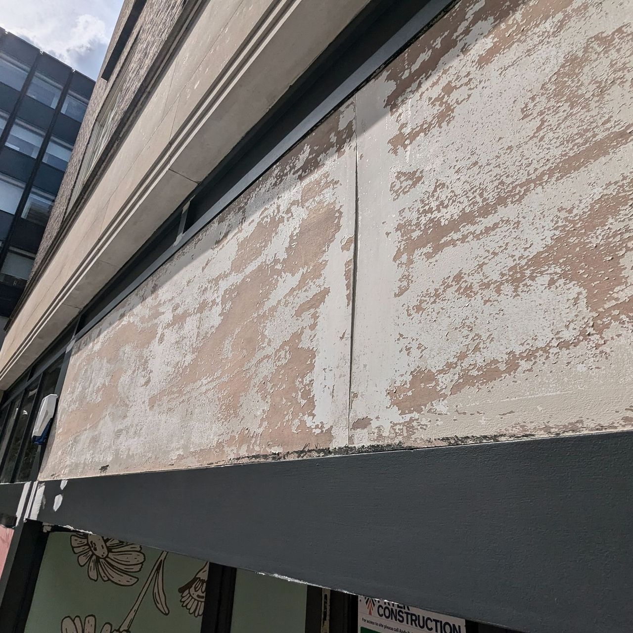A shopfront fascia stripped back to patchy bare substrate above a dark painted spandrel panel