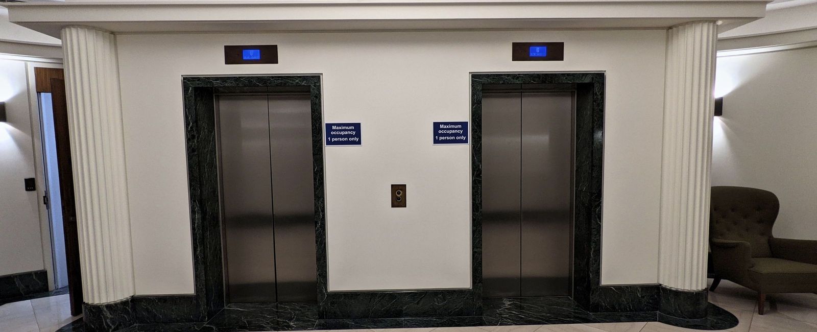 Lift lobby with two lifts in green marble surrounds, fluted pilasters and the terrazzo roundel in the foreground